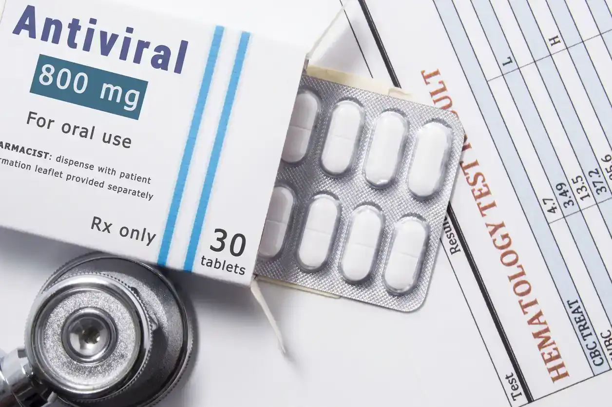 Antiviral drug. Open paper packaging box of medication with name group of drug Antiviral, blister with pills, next to stethoscope and blood test results.