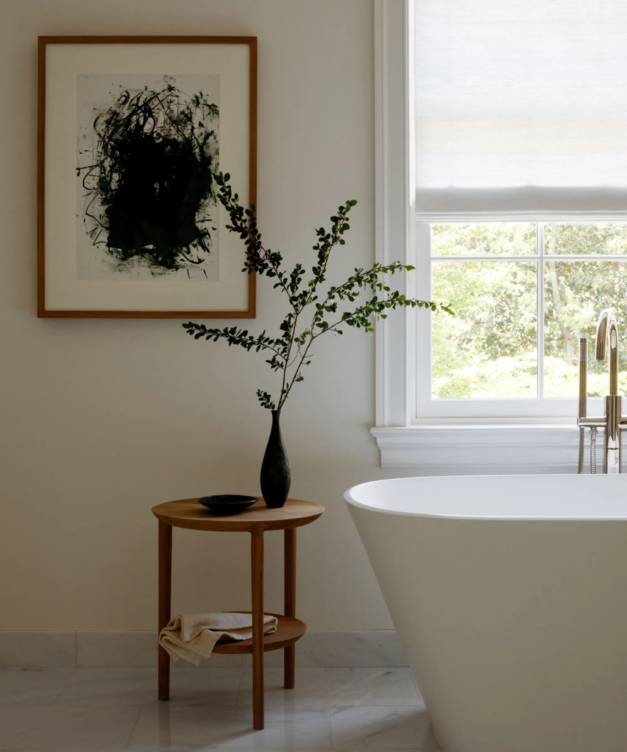 Um banheiro neutro em forma de spa com paredes brancas quentes piso de azulejos de uma banheira independente branca e uma mesa lateral de madeira coberta com um vaso cheio de vegetação' loading='lazy' title=