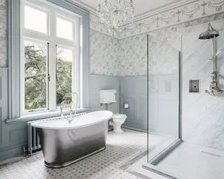 Un baño con lámpara de araña, bañera independiente y papel pintado azul y blanco.