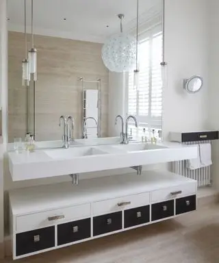 Un baño neutro con un tocador doble blanco y una gran lámpara de araña esférica blanca.