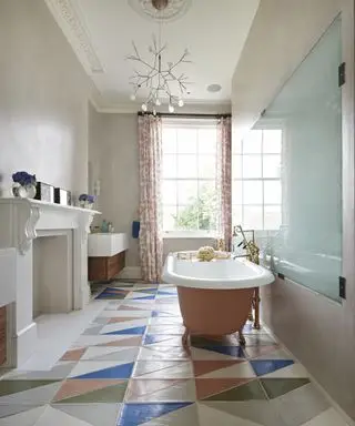 Un baño con paredes rosas y bañera independiente, lámpara de araña contemporánea y suelos de baldosas.