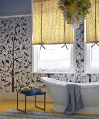 Un baño con papel pintado estampado en amarillo y azul y una lámpara de araña de cristal soplado.