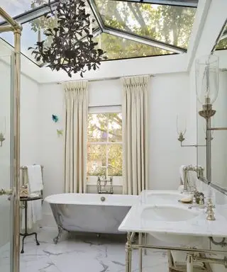 Un baño blanco con lámpara de araña negra y techo de cristal.
