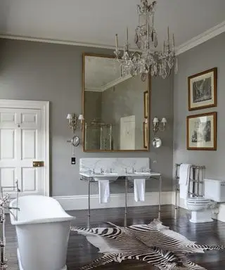 Un baño gris con lámpara de araña de cristal y alfombra de animales.