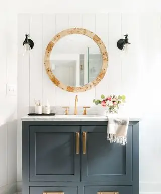 Salle de bains avec lambris à feuillures blancs et meuble-lavabo gris foncé avec miroir de salle de bains circulaire et éclairage mural