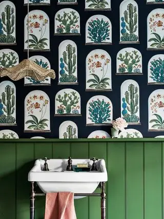 Un tocador con paneles de pared verdes detrás de un lavabo blanco y debajo de papel tapiz botánico