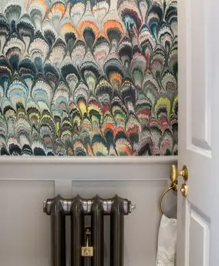Un tocador con papel pintado estampado multicolor, un pequeño radiador negro y una toalla de mano blanca.