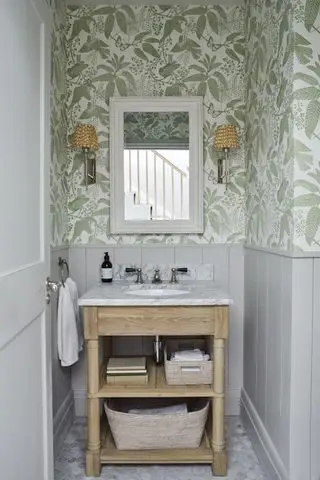 Un tocador luminoso con un lavabo de madera con estantes abiertos, paneles de pared grises y papel tapiz botánico verde y blanco.