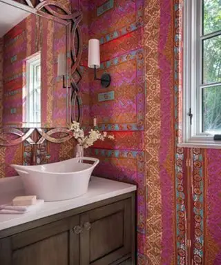 Un ejemplo de decoración de pared de tocador que muestra un tocador de color rosa brillante con un soporte de lavabo de madera y un lavabo blanco.