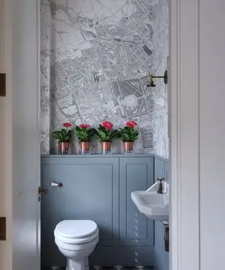 Un tocador de color gris claro con artículos sanitarios blancos y papel tapiz con mapas en blanco y negro sobre paneles grises.