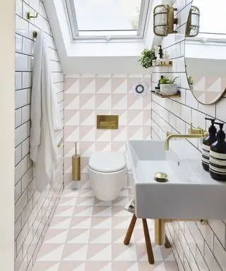 Un ejemplo de ideas para pisos de baños pequeños que muestran pisos y paredes geométricos en rosa y blanco con un lavabo blanco y herrajes dorados.