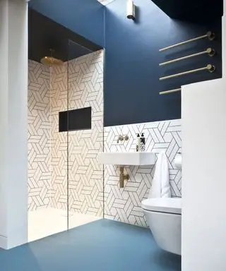 Un ejemplo de ideas de pisos para baños pequeños que muestran pisos de ducha azules y azulejos blancos con lechada negra.