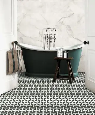 Un baño independiente de color verde oscuro frente a azulejos de mármol y pequeños mosaicos en blanco y negro