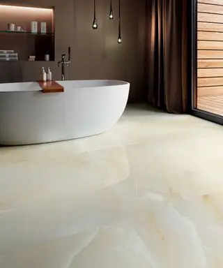 Un ejemplo de ideas de pisos para baños pequeños que muestran baldosas de porcelana de efecto piedra y una gran bañera blanca independiente frente a una pared marrón.