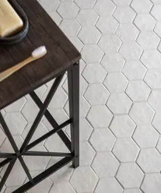 Un primer plano de pequeñas baldosas hexagonales blancas debajo de una mesa de madera con un cepillo de dientes