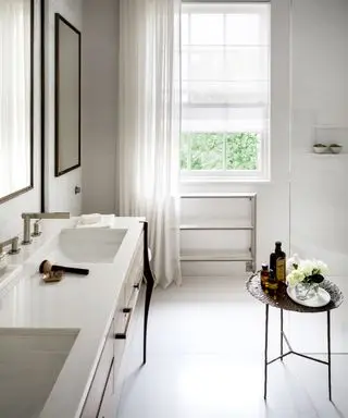 Baño totalmente blanco, azulejos de mármol, paredes pintadas de blanco, suelo de baldosas blancas, mesa auxiliar metálica