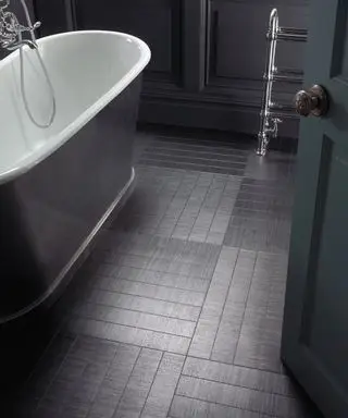Suelo de vinilo negro en baño con bañera blanca y gris, paredes pintadas de negro