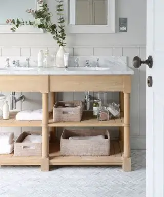 Cuarto de baño con suelo de baldosas en forma de espiga, mueble de madera clara con lavabo, encimera de mármol y cestas de almacenaje