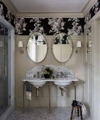 Salle de bain avec meuble vasque en marbre veiné, carrelage en marbre au sol, papier peint fleuri et boiseries peintes