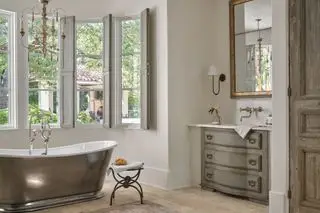 Élégante salle de bains de style français avec volets, baignoire sur pieds, meubles anciens et lustre