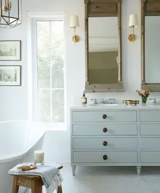Salle de bain blanche élégante avec miroirs anciens, appliques murales en laiton et meuble vasque bleu clair