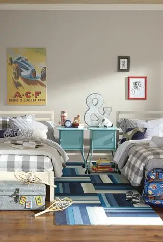 חדר שינה משותף לילדים כחול ואפור עם שפע של דפוסים, כולל מצעים בצבע אפור, ארונות ליד המיטה בצבע כחול בהיר ואמנות קיר צבעונית.