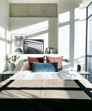 Eine Idee für ein Schlafzimmer in einer Wohnung mit Kissen in Ocker- und Blaugrüntönen und Kunstwerken auf einem Regal