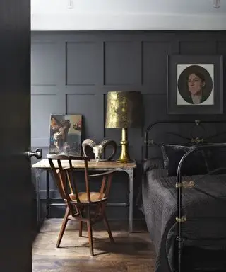 Ein Schlafzimmer mit schwarz gestrichenen getäfelten Wänden, einer weißen Decke und Holzböden