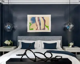 Ein Hauptschlafzimmer, das Schlafzimmerideen für Apartments mit marineblauen, glänzend gestrichenen Wänden und auffälligen Kunstwerken, einschließlich einer Skulptur am Ende des Bettes, demonstriert