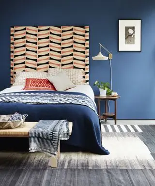 Beispiel für Aufbewahrungsideen für ein Apartmentschlafzimmer mit dunkelblauen Wänden, einem gemusterten orange-blauen Kopfteil und einem blau-weißen gewebten Teppich