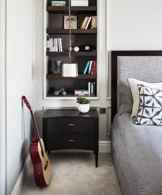 Eingebaute offene Regale neben dem Bett, über einem schwarzen Beistelltisch mit Schubladen, die Ideen für ein Apartment-Schlafzimmer demonstrieren.