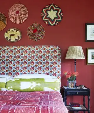 parete rossa della camera da letto con testiera fantasia e cesto colorato esposto sulla parete