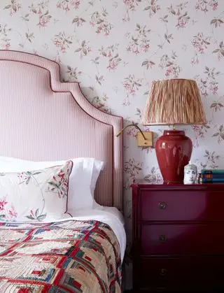camera da letto con testiera a righe rosse, cassettiera rossa, lampada rossa, carta da parati con petali rossi, plaid vintage