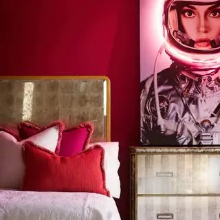 camera da letto rossa con letto dal bordo dorato e cassettiera abbinata, opere d'arte moderna, cuscini con frange