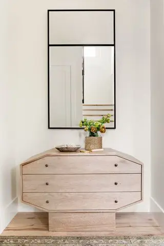 commode de chambre à coucher dans une alcôve avec miroir au-dessus, vase de fleurs, tapis, bol à bibelots