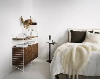 rangement modulable dans une chambre, rangement avec quatre tiroirs et étagères, fixé au mur, table d'appoint noire, lit avec literie blanche, peau de mouton et oreillers marron