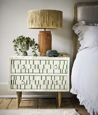 chambre avec table de nuit incrustée d'os en vert et crème, lit rembourré avec couverture à carreaux, lampe de table dorée, plante, parquet