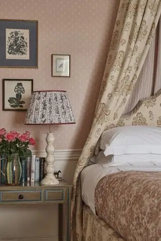 Lit et table de chevet traditionnels rose/pêche avec tissus floraux, y compris sur une lampe, illustrant comment agrandir une petite chambre