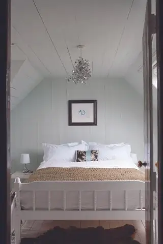 Comment agrandir une petite chambre dans une chambre vert pâle dans un grenier avec des boiseries et un lit double blanc
