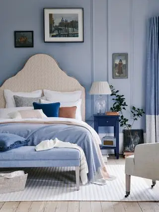 Chambre bleue avec tête de lit haute et table d'appoint avec lampe allumée, illustrant comment agrandir une petite chambre