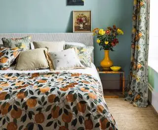 Chambre bleue avec lit bas, citrons sur la literie et rideaux fleuris, démontrant comment agrandir une petite chambre.