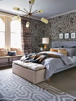 Un esempio di idee per un lampadario in camera da letto che mostra un letto grigio e un tappeto a motivi grigi e bianchi sotto un lampadario Sputnik