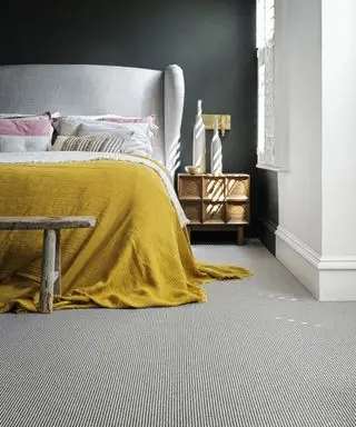 Un dormitorio con paredes negras, una cama blanca con una manta amarilla y una alfombra a rayas blancas y negras.
