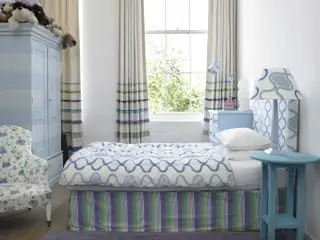 dormitorio para adolescentes con rayas azules y estampados gráficos, cómoda azul, mesa auxiliar azul, lámparas azules y armario con rayas azules