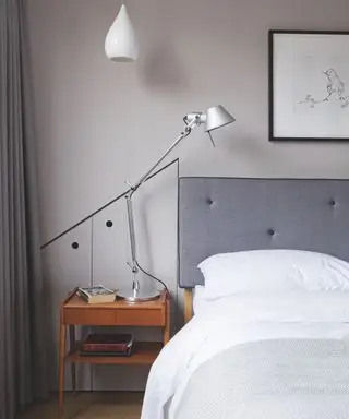 Una idea de dormitorio para adolescentes con cabecera tapizada en gris, paredes de color gris cálido, mesita de noche de madera y lámpara angular.