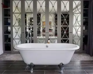 Baño blanco con patas en el dormitorio con un gran armario con puertas de espejo, mezcla de alfombras y suelos de madera