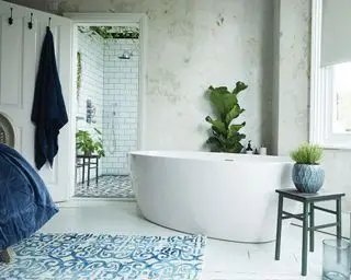 Dormitorio contemporáneo, luminoso y luminoso con baño en la esquina de la habitación, paredes blancas texturizadas, suelos de madera pintados de blanco, jarrones decorativos azules, alfombras y ropa de cama, con vistas al baño privado.