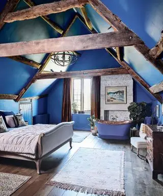 Dormitorio con techo abovedado, paredes azules y baño independiente de cobre y azul en una casa de campo de Cotswolds del siglo XII.