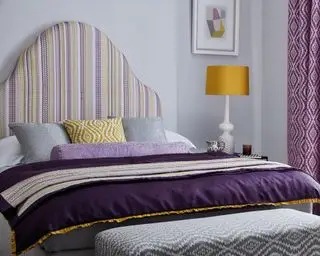 Chambre peinte en lilas avec une grande table de chevet et des rideaux violets