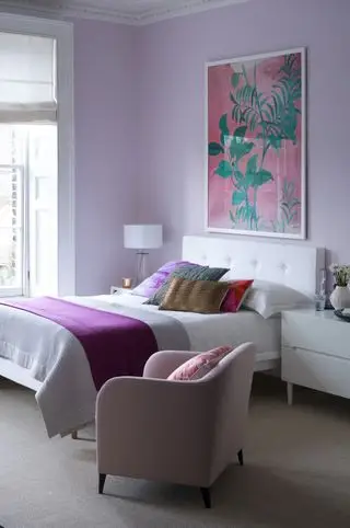 Chambre lilas avec œuvres d'art, linge de lit blanc et coussins colorés